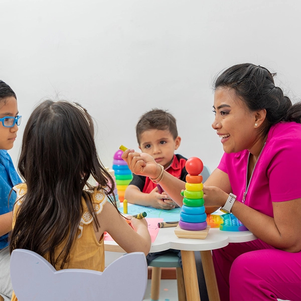 Female pediatrician sitting at a table with several children playing in her medical office